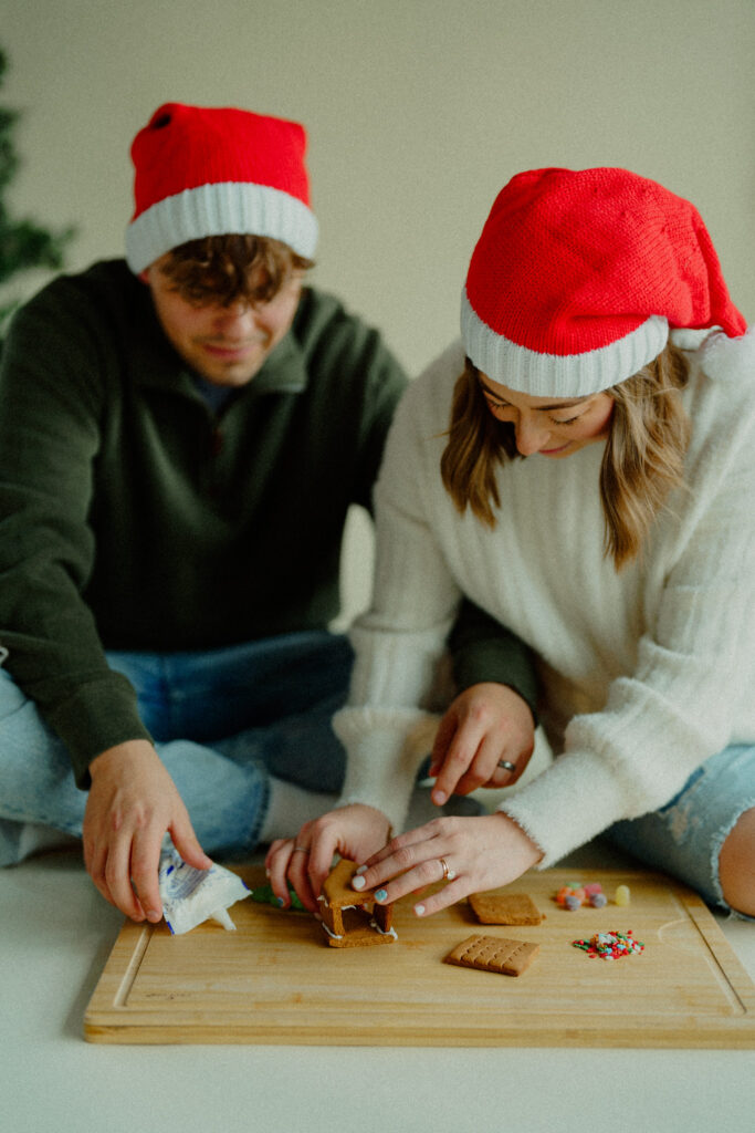 Expecting couple decorating a gingerbread house together  putting the little pieces together