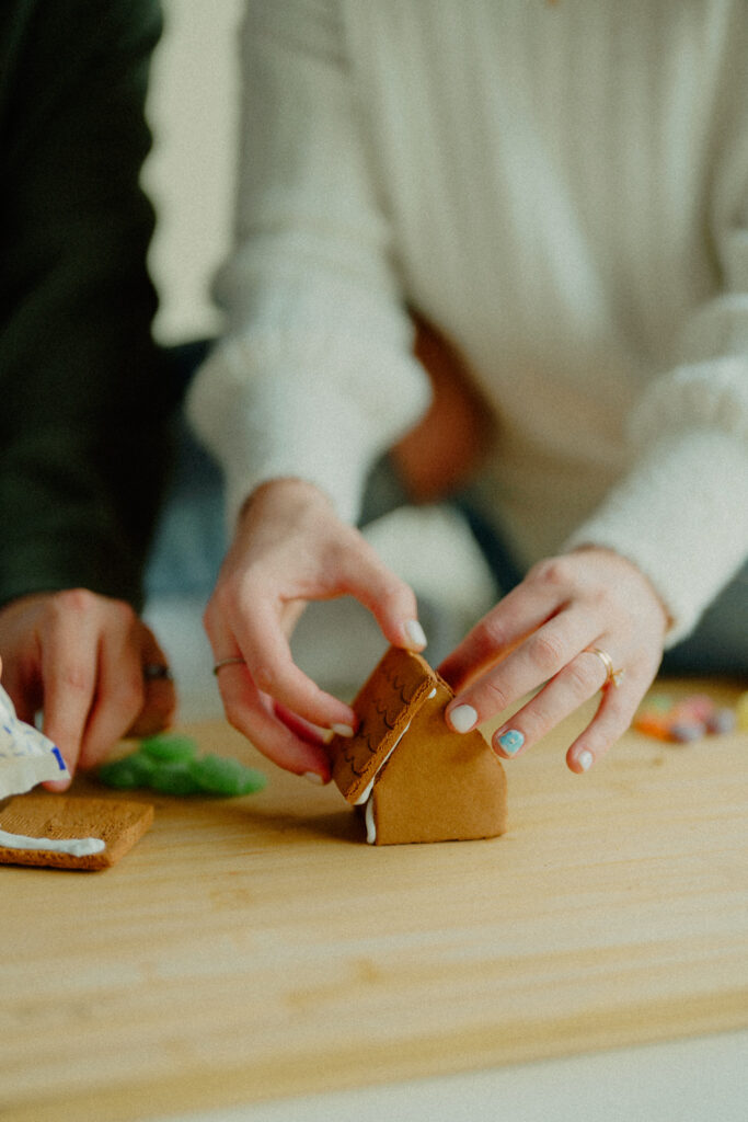 Expecting couple is putting together the pieces of a gingerbread house