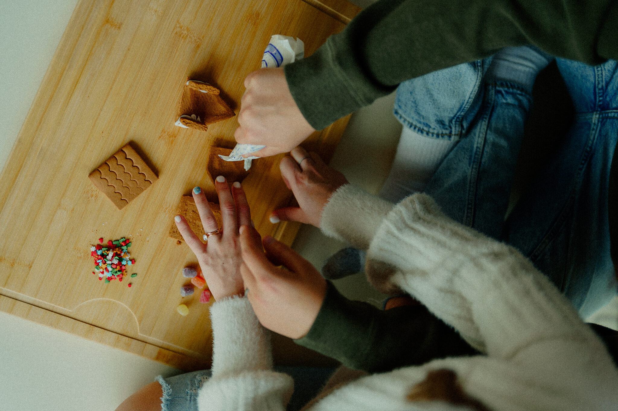 cozy christmas photos - couple decorating a gingerbread house with the photo captured from their point of view looking down