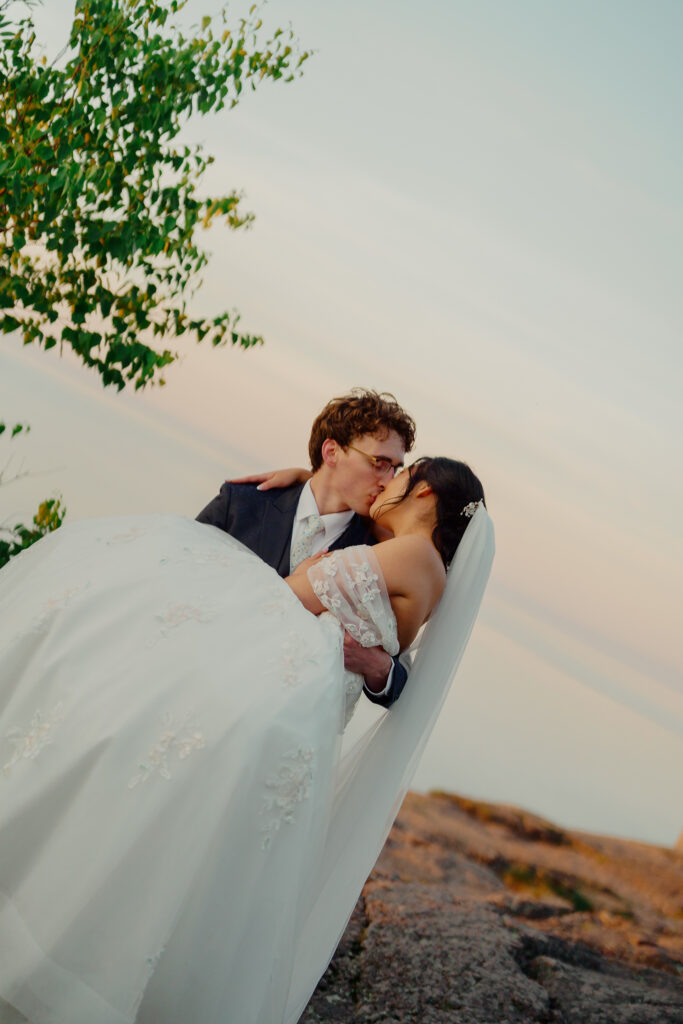 Eloping couple kissing while groom holds bride in his arms