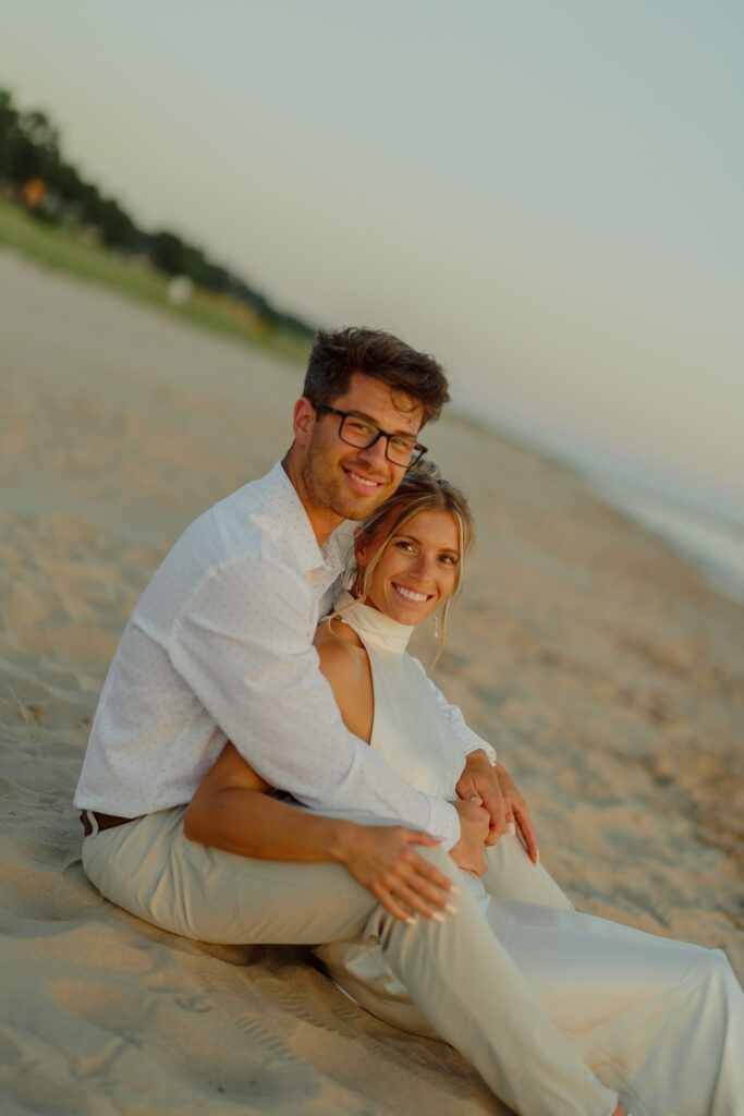 Couple sitting in the sand and smiling at the camera