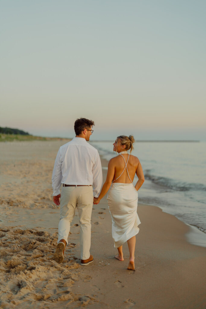 Couple holding hands and walking on beach smiling at each other