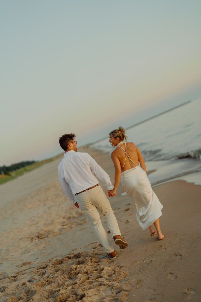 Couple holding hands and walking on beach walking off into the sunset
