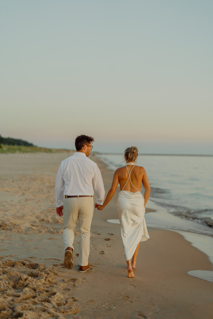 Couple holding hands and walking on beach view of their backsides