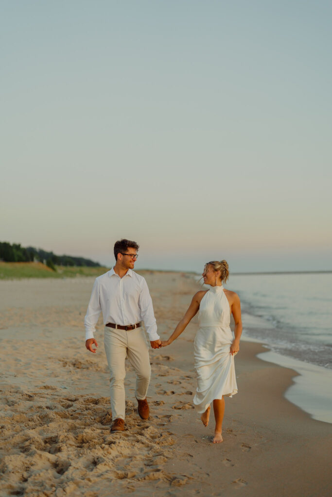 Couple holding hands and walking on beach smiling at each other