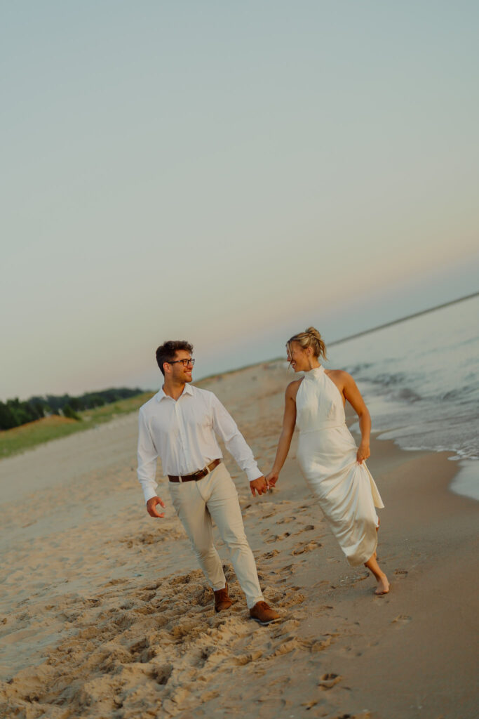 Couple holding hands and walking on beach smiling at each other