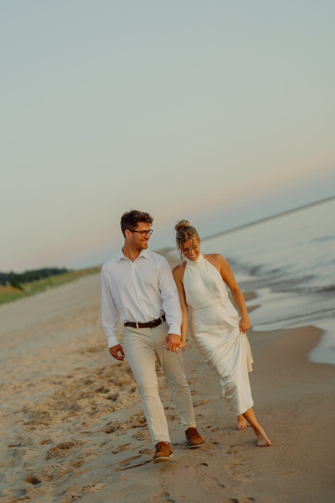 Couple holding hands and walking on beach smiling