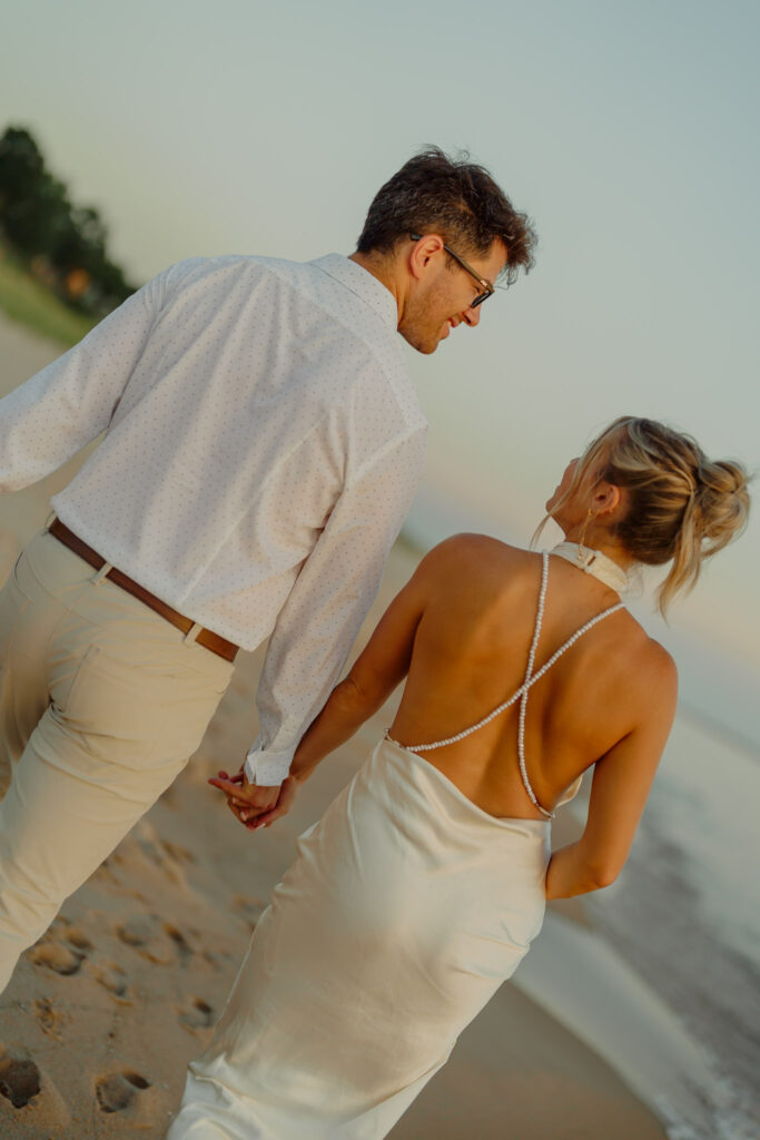 Couple holding hands and walking on beach and smiling at each other