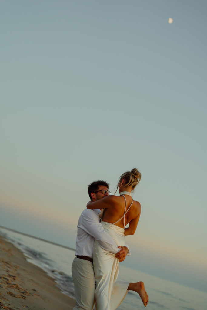 Man spins woman as he is holding her up in the air on the beach