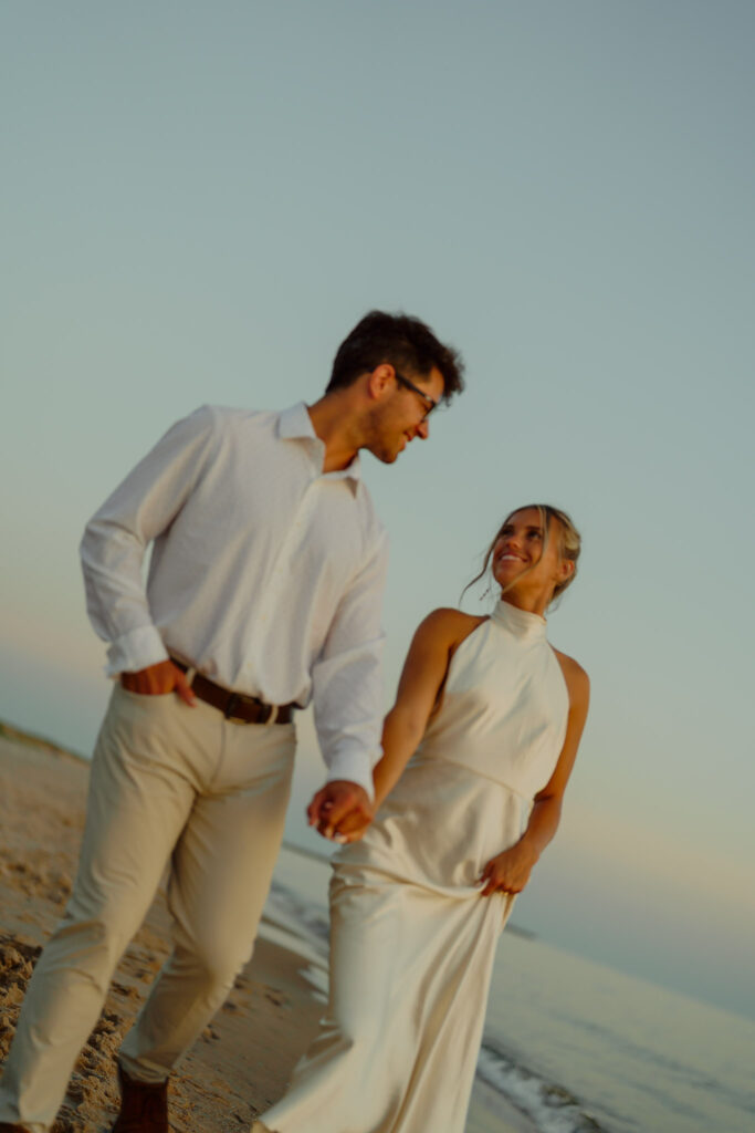 Couple holding hands on the beach and smiling at each other