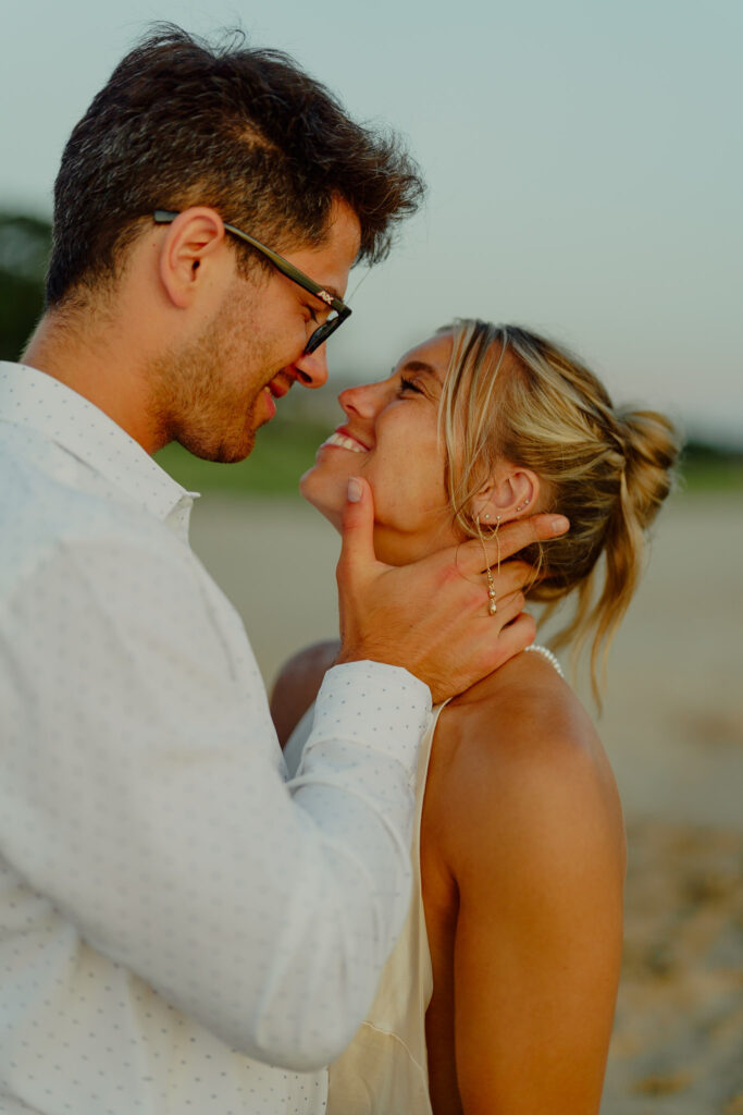 man holding his hand against womans neck lightly and smiling at her