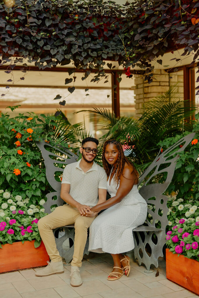 Engagement photos in Powell Gardens butterfly room, couple smiling at camera and holding hands