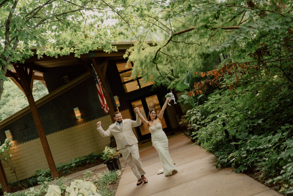 Overland Park Arboretum & Botanical Garden entrance, wedding photo couple walking out hand in hand with their fists up in celebration